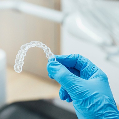 Dentist with blue gloves holding clear aligner