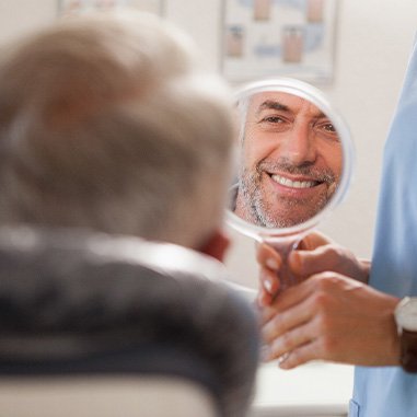 Man smiling at reflection in handheld mirror