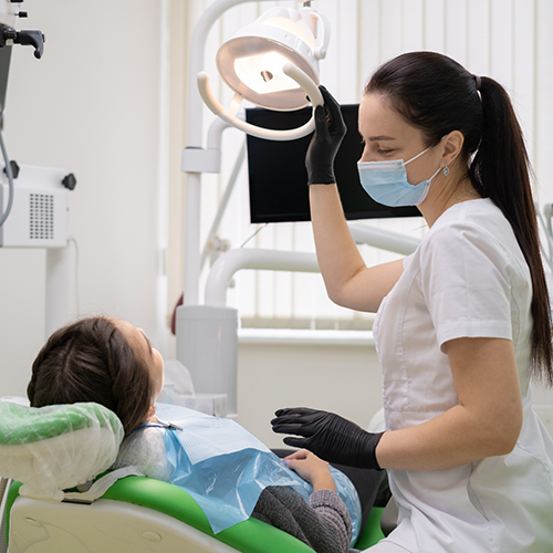 Female dentist with mask shining dentist on patient's mouth