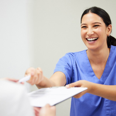 Smiling dental assistant handing patient forms