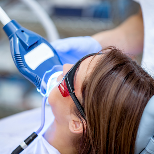 Woman sitting back in dental chair receiving teeth whitening