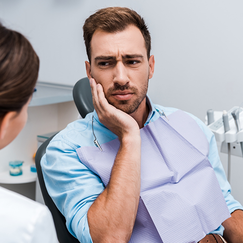 Man sitting in dental chair rubbing jaw in pain