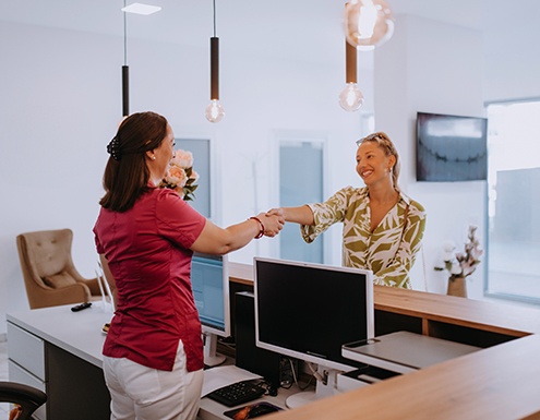 Smiling dental receptionist and patient shaking hands