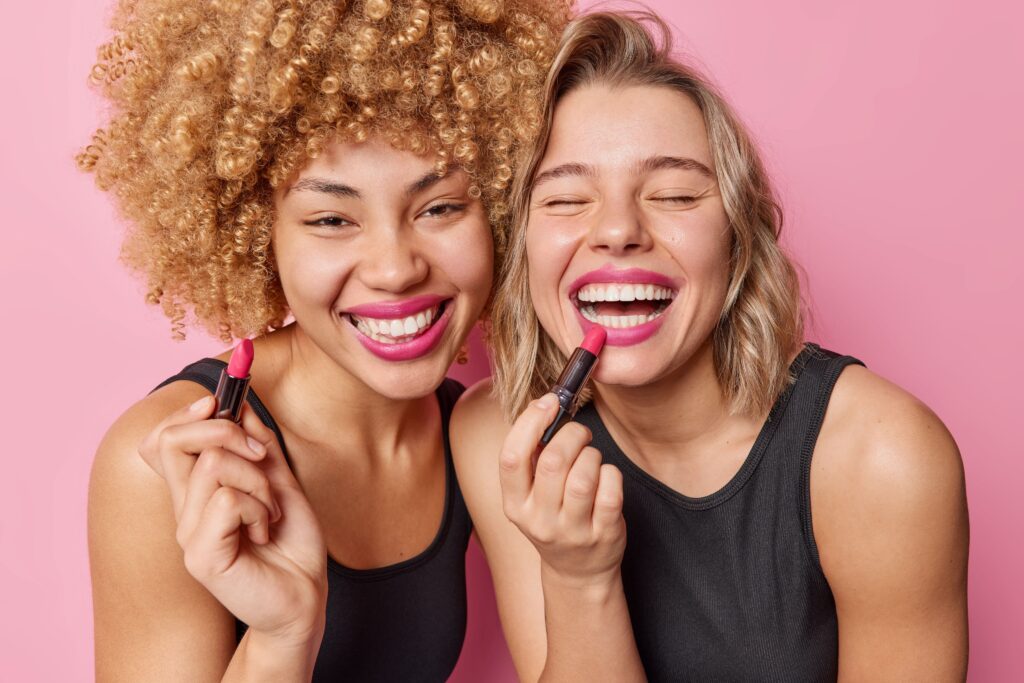 Two woman laughing and applying lipstick
