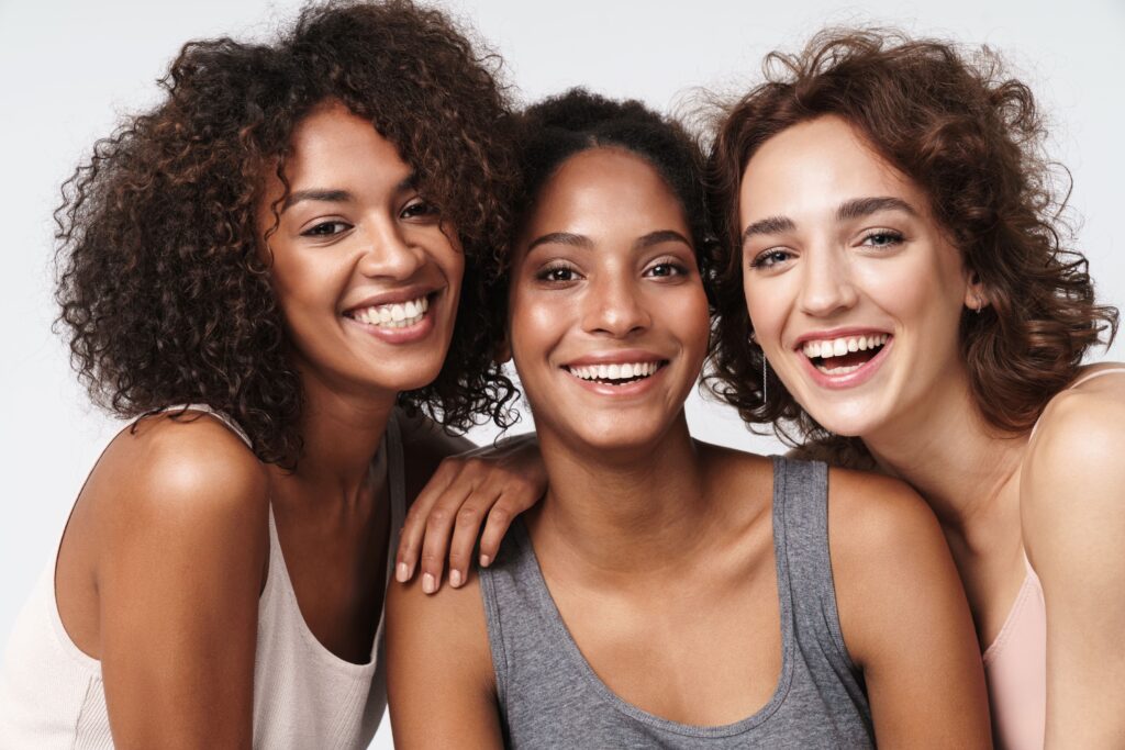 Three young women leaning on each others' shoulders smiling